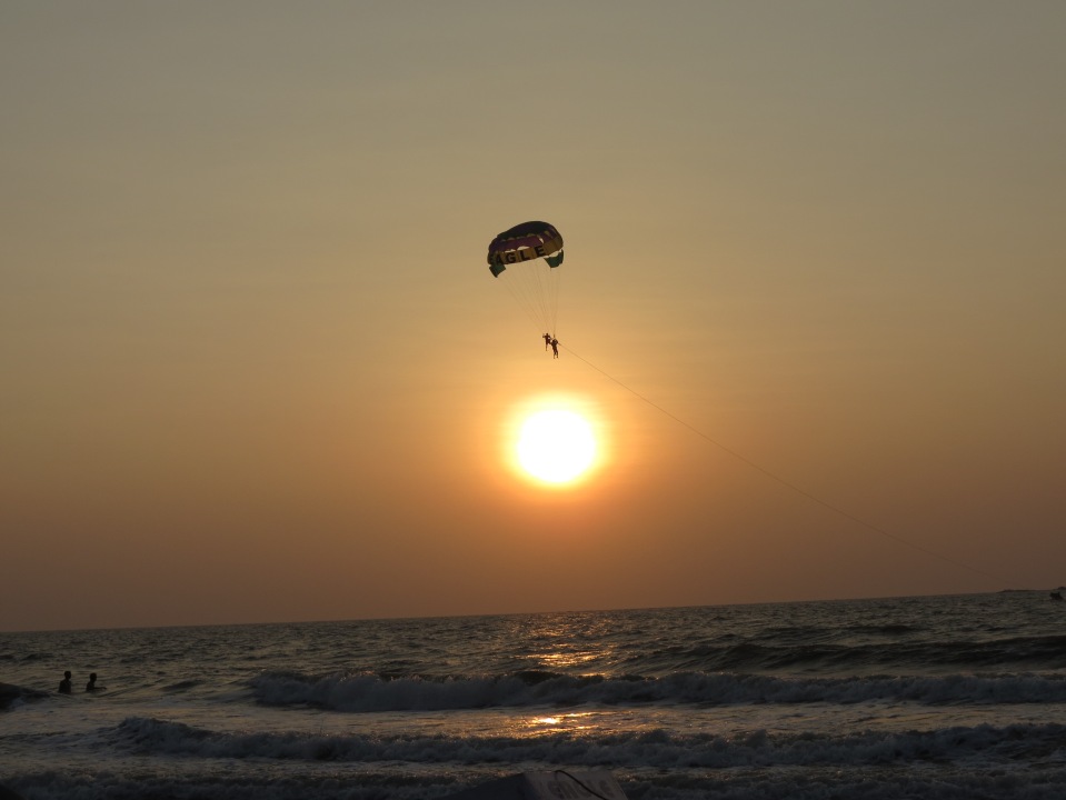 A lone parasailing expedition overlooks the setting sun as it embarks on a journey with the waves unfurling beneath.